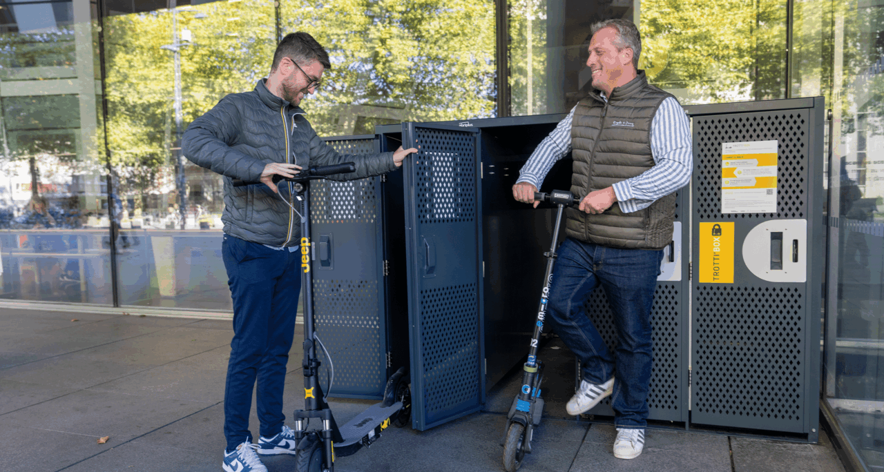 Personnes qui rangent une trottinette dans la Trottin'Box AbriPlus