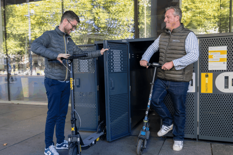 Personnes qui rangent une trottinette dans la Trottin'Box AbriPlus